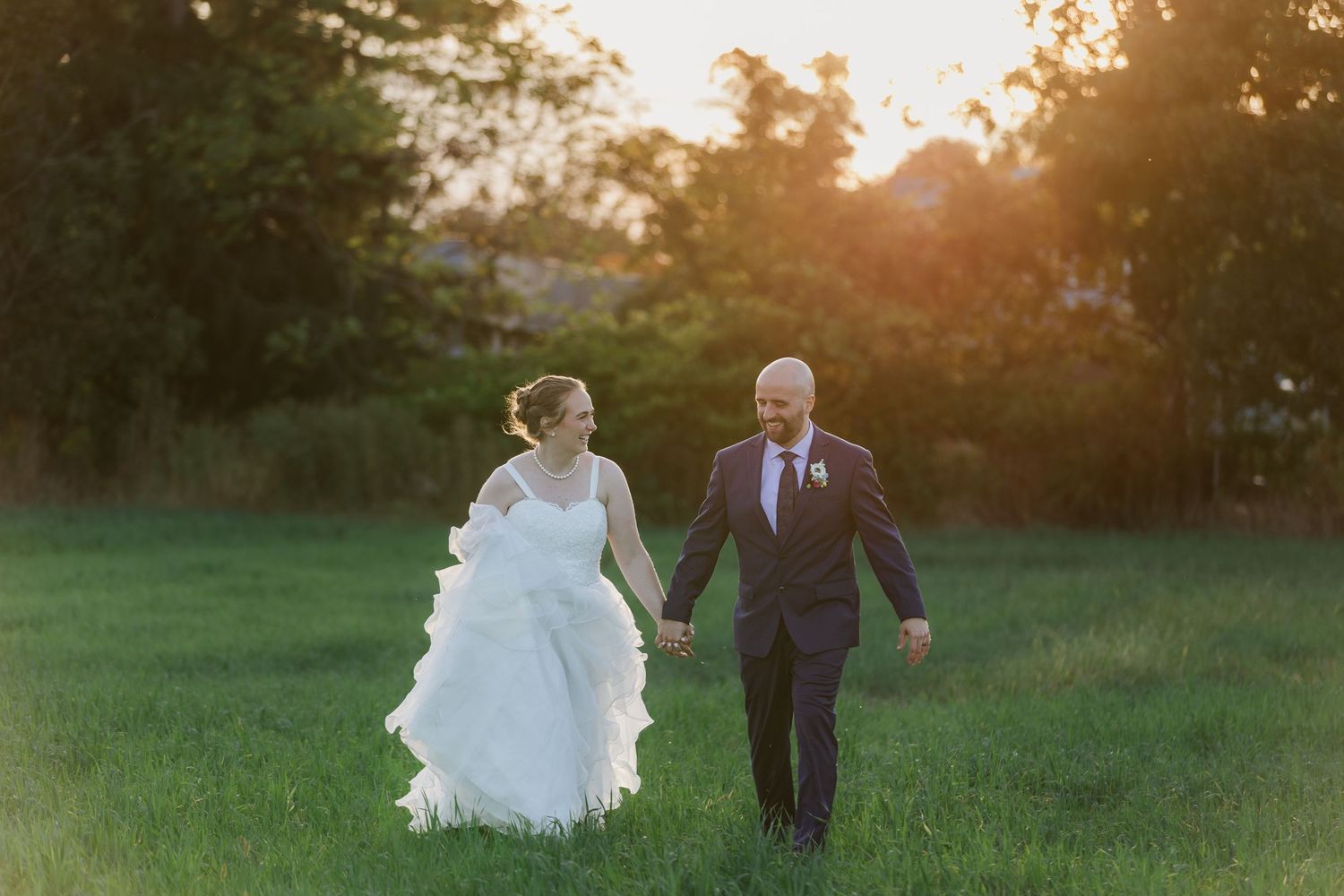 Bride and groom walking through a field for their sunset wedding photos near woodstock, ontario.