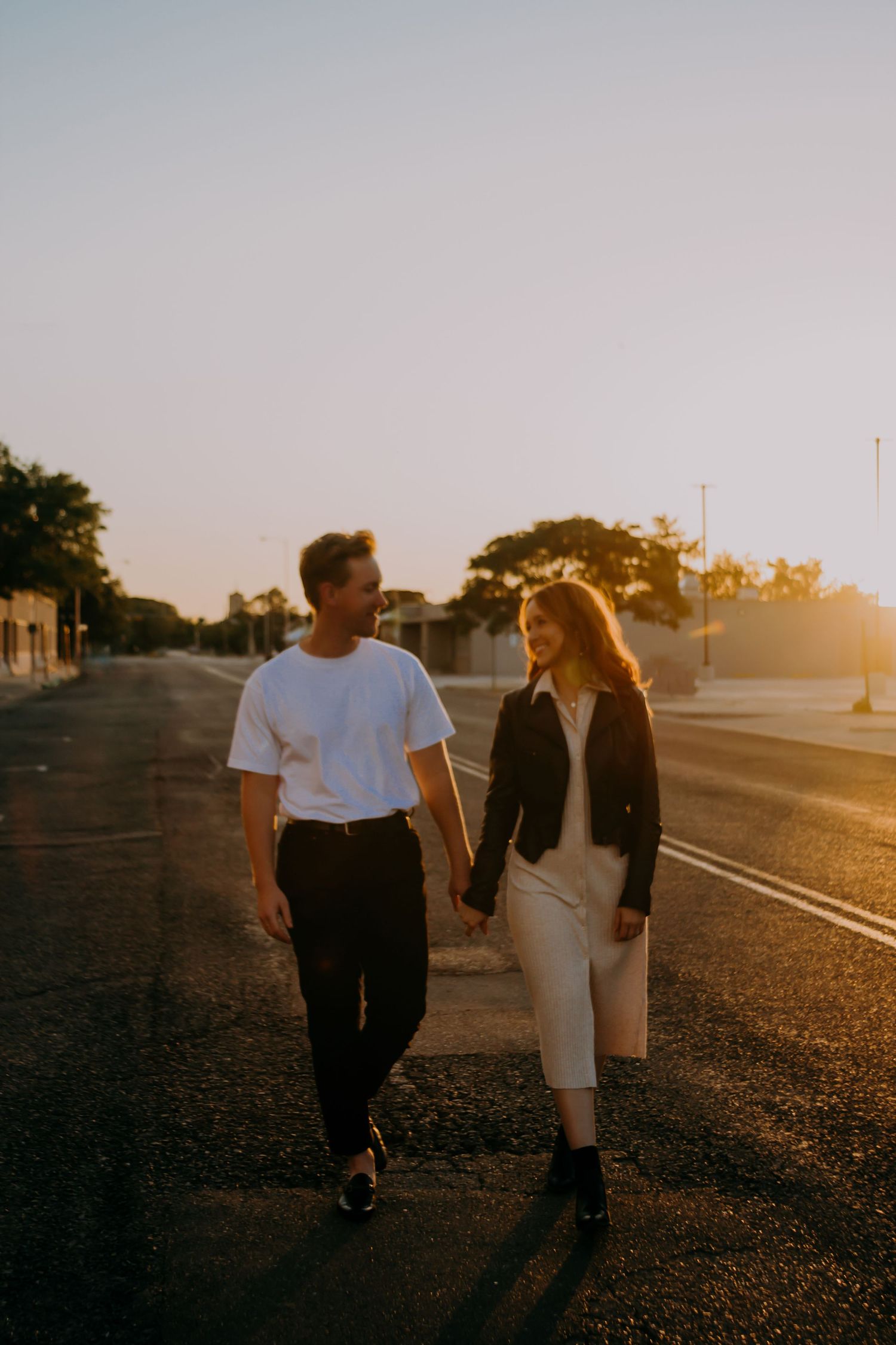 Couple holding hands walking on road at golden hour sunset.