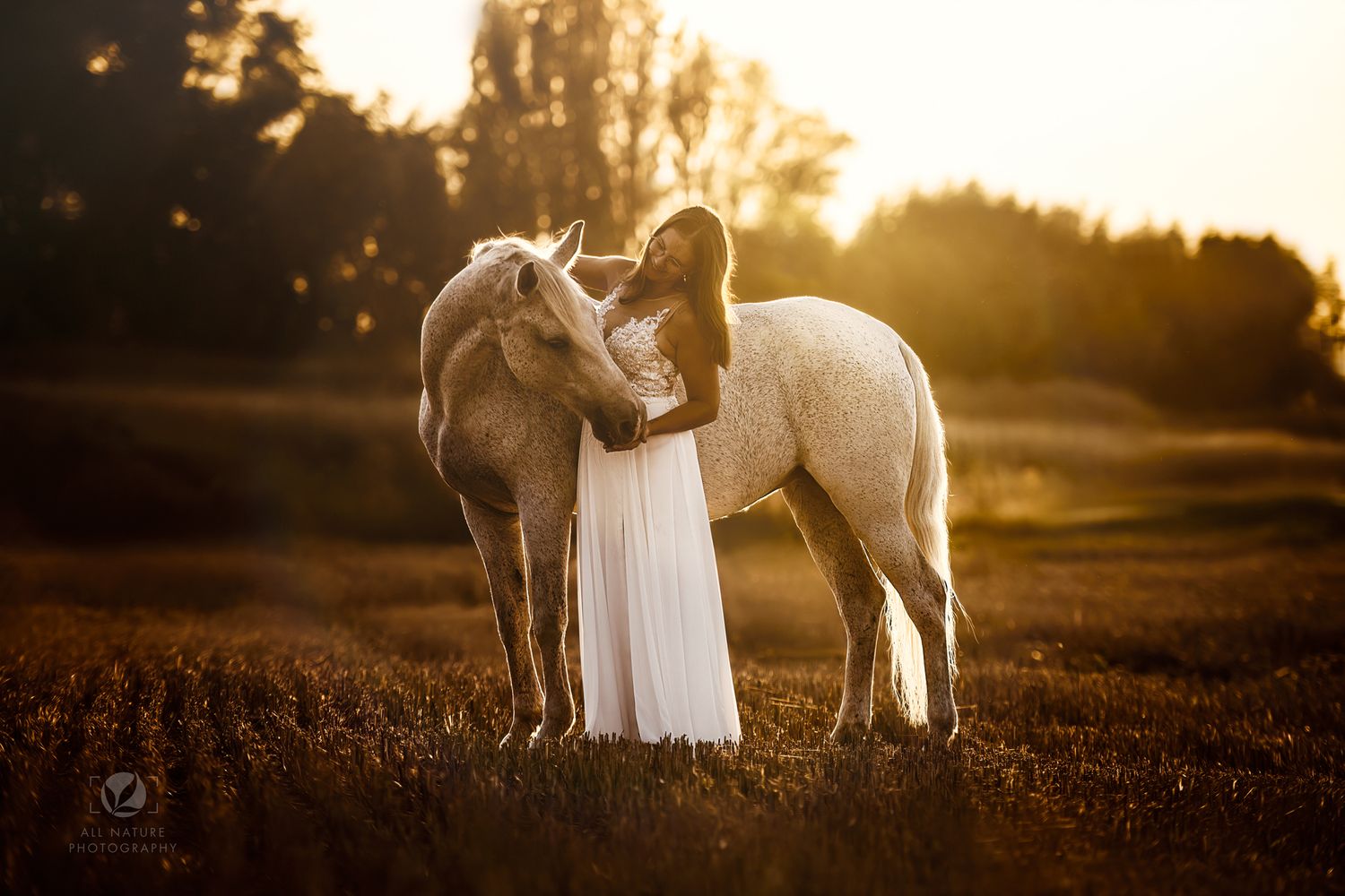 Two white horses nuzzling with figure in flowing dress at golden sunset.