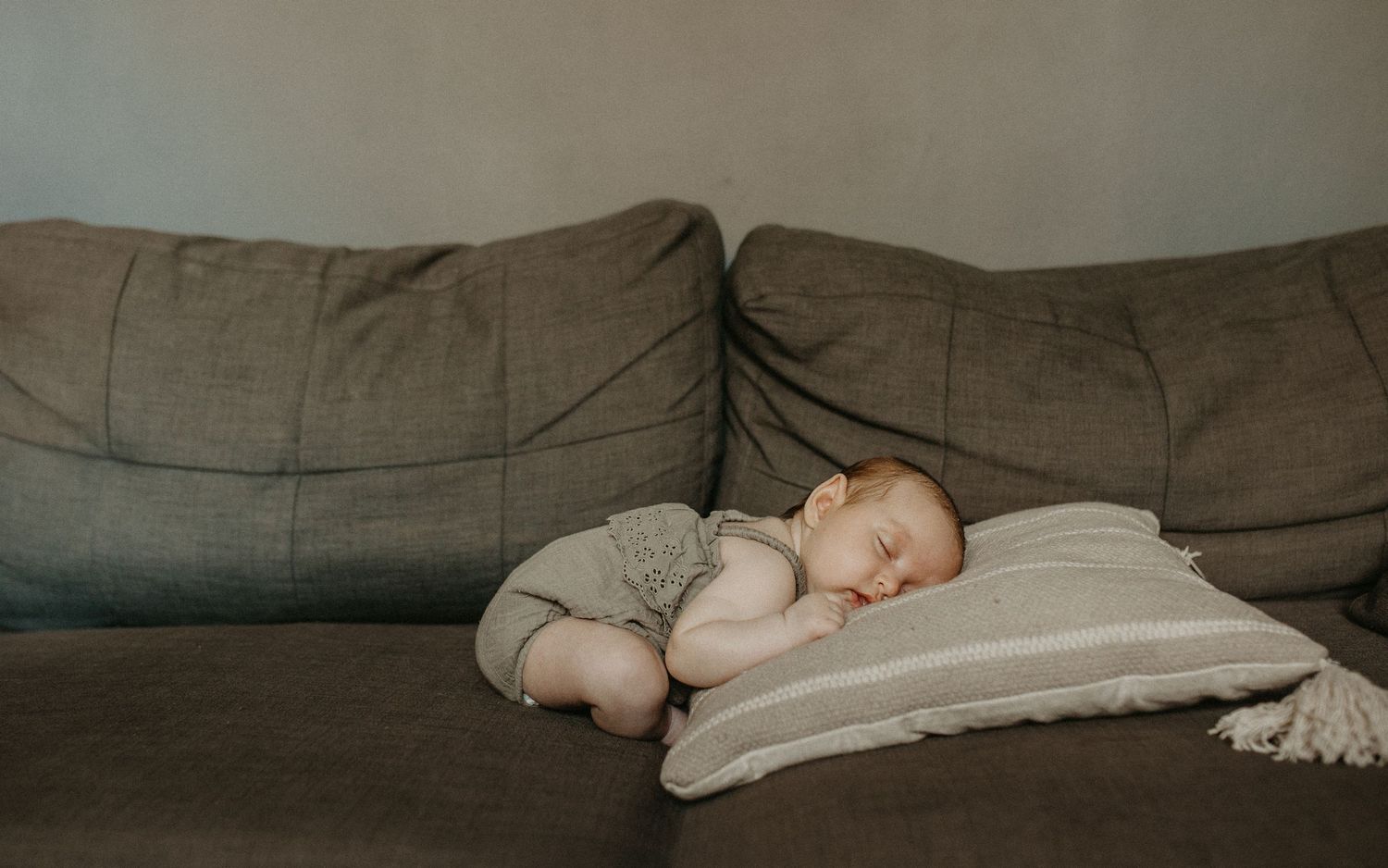 A baby sleeping peacefully on a grey couch, captured in a series of connected photos showing different angles.Newborn photographer london