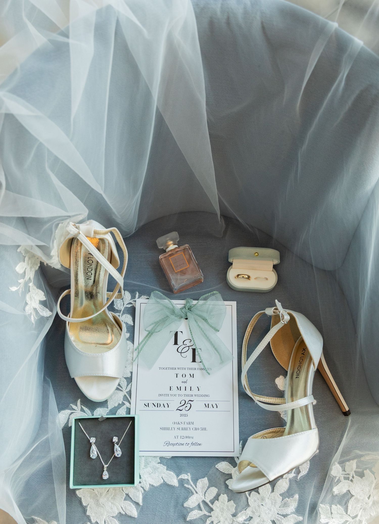 Elegant wedding details featuring white tulle fabric, jewelry, and invitation cards arranged in a soft, ethereal composition.
