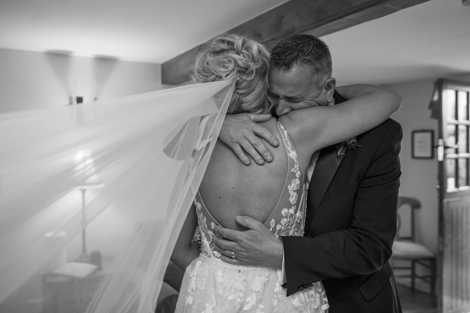 A tender black and white wedding moment captured as a couple shares a romantic embrace under a flowing veil.