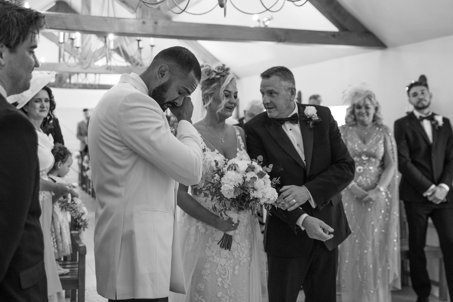 Wedding guests gather in formal attire to celebrate and applaud during an indoor reception ceremony.