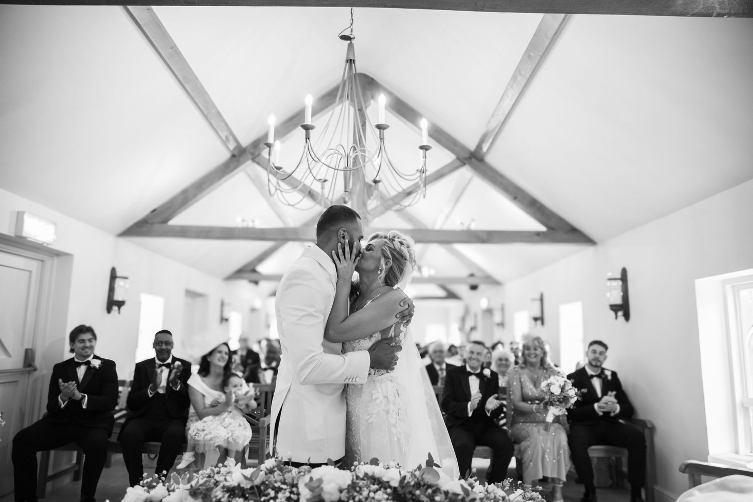 Black and white photo series showing wedding celebration moments in a bright reception venue with vaulted ceilings.