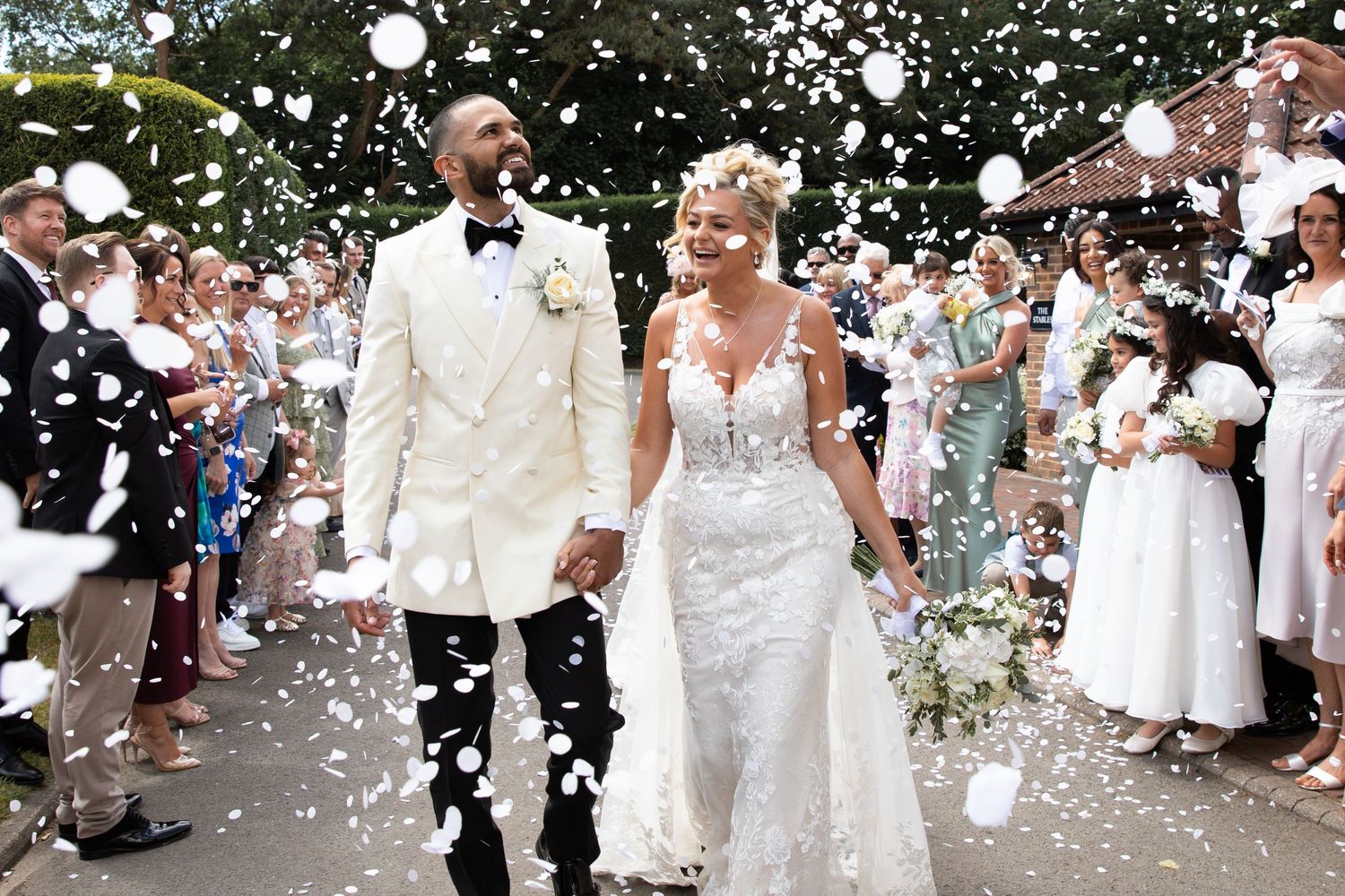 Wedding guests celebrate by throwing white flower petals as newlyweds walk through a joyful outdoor celebration.