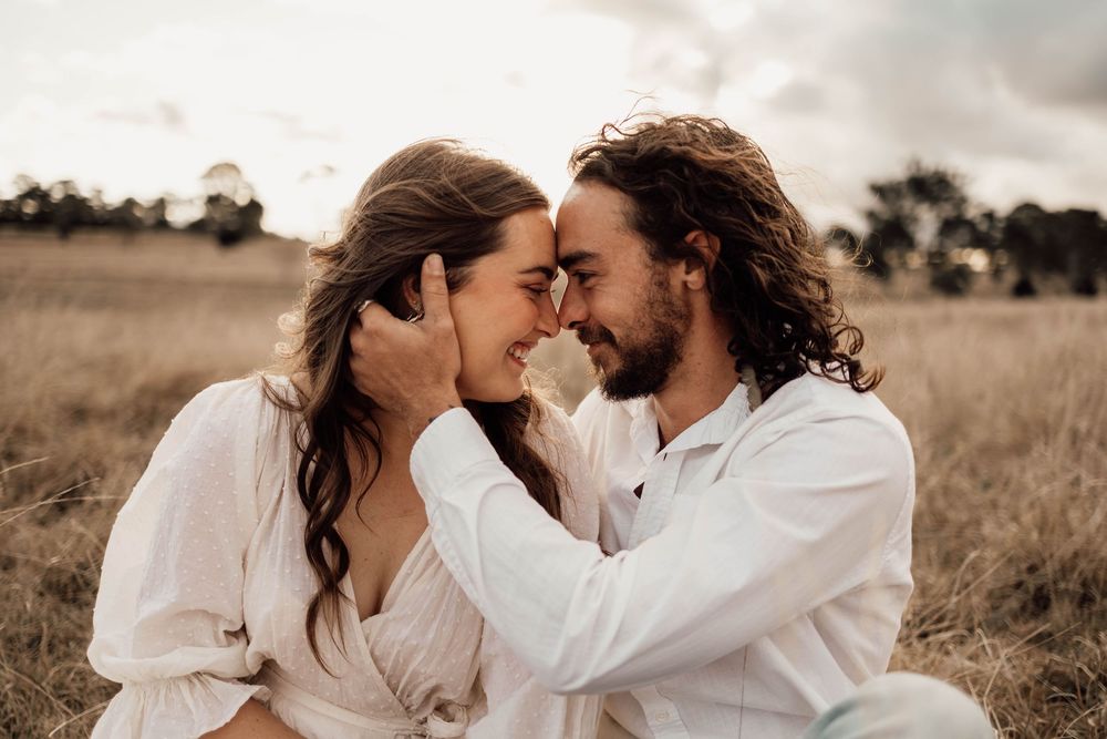 Romantic couple in white clothing sharing intimate moments in a rustic outdoor field setting.