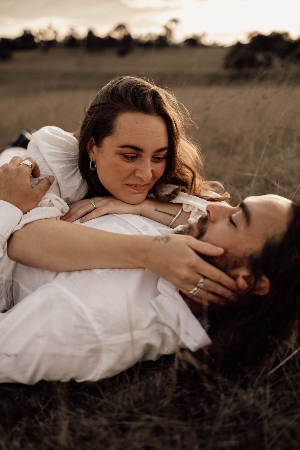 Couple in white clothing lying together in tall grass during golden hour.