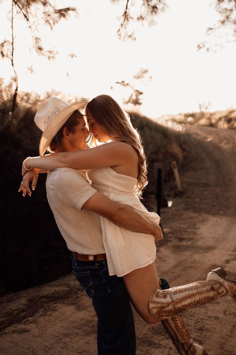 A romantic couple embraces in warm sepia tones outdoors during a sunset photoshoot.