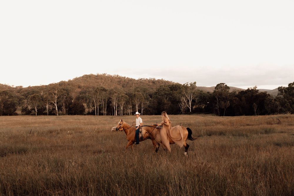 Two horses and riders traverse a golden autumn field at sunset with trees lining the horizon.
