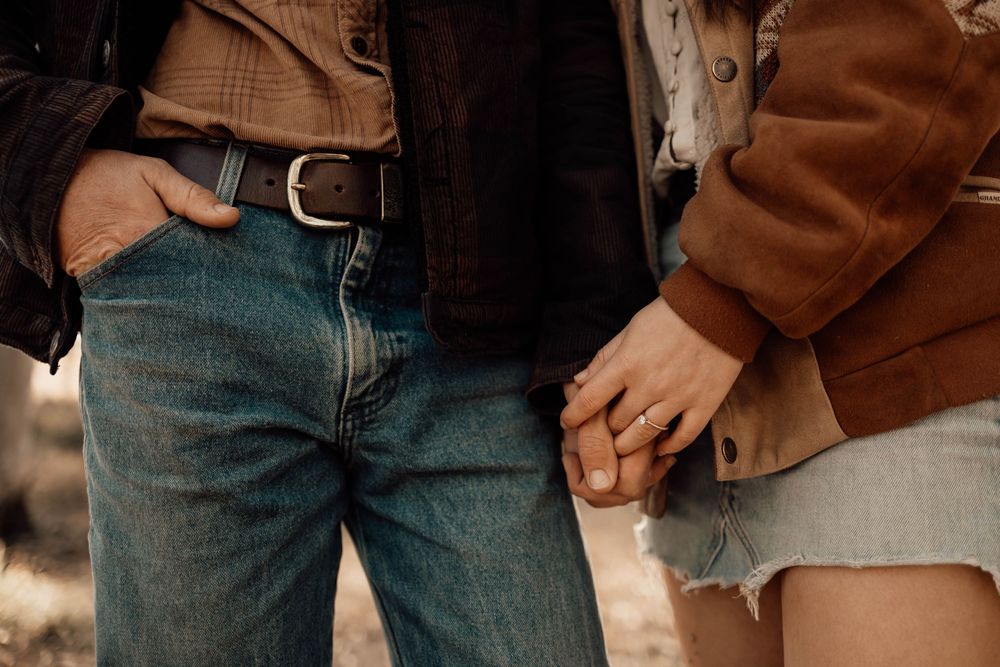 Close-up fashion details of brown leather jacket paired with blue denim jeans in a casual style.