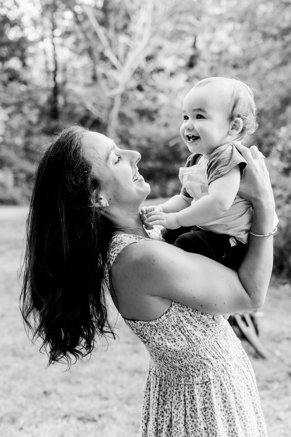 A joyful black and white photo series showing a parent lifting and playing with a small baby outdoors.
