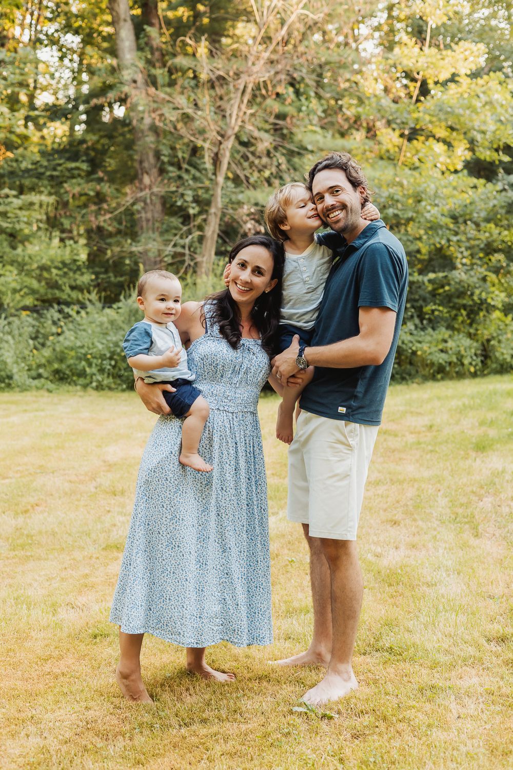 A family enjoys a playful moment together on a sunny day in a grassy outdoor setting.