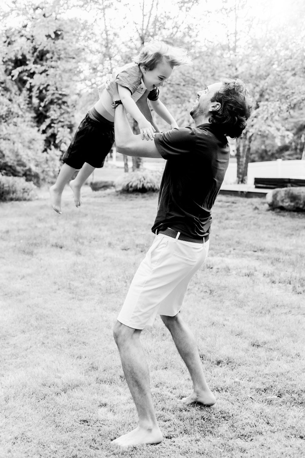 A black and white photo showing a playful moment lifting a child in a backyard garden setting.