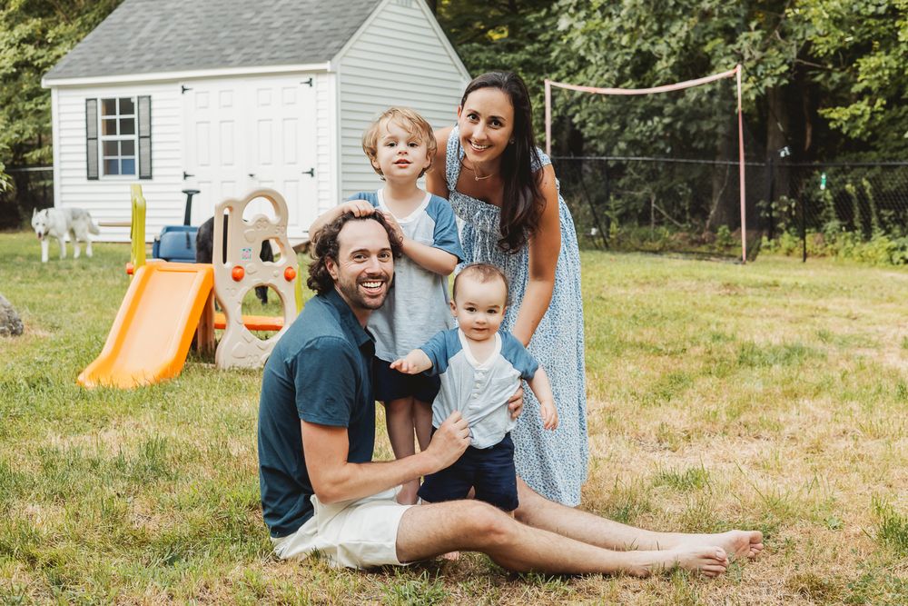 A family enjoying time together in their backyard with playground equipment and a white shed in the background.