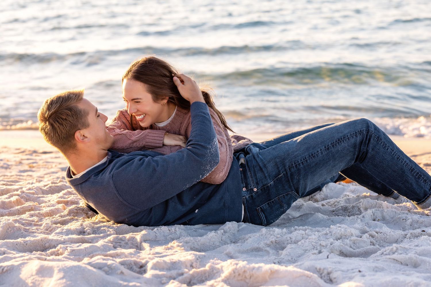 Romantic couple lying together on a sandy beach at sunset sharing intimate moments by the ocean waves.