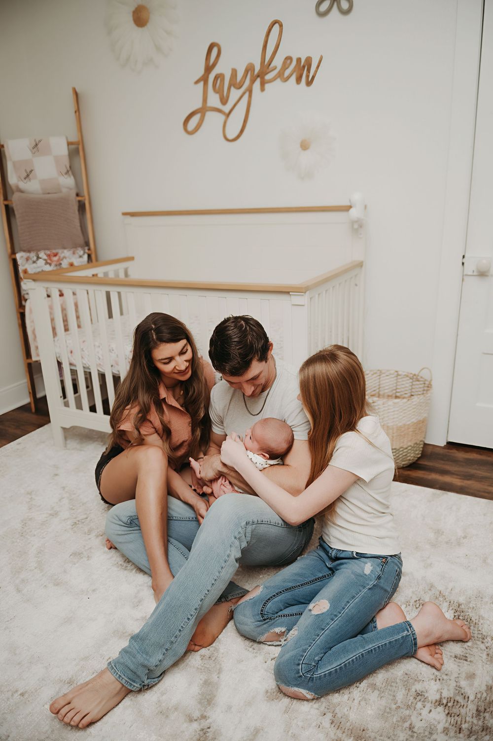A cozy nursery scene with a group sitting on a plush carpet near a white crib, with 'Layken' written on the wall.