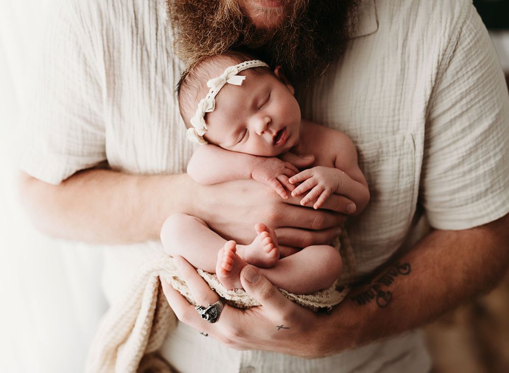 Close-up series of a sleeping newborn baby being gently cradled in soft white blankets.