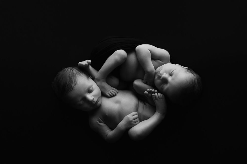 A series of black and white artistic photographs showing intimate moments of sleeping twin babies in various poses.