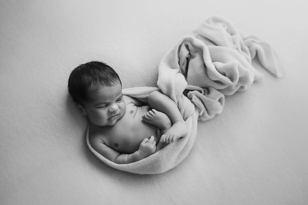 Black and white newborn photo of a sleeping baby wrapped in a soft blanket, curled in a peaceful pose.