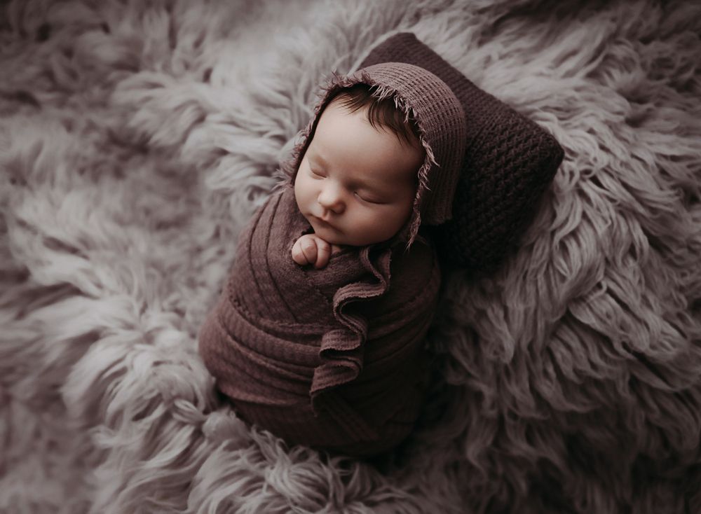 Newborn baby in purple wrap snuggled up by Jessica Rae Portraits.