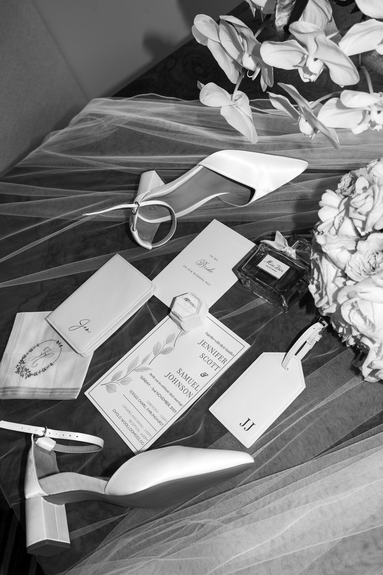 Wedding stationery and invitations arranged with white flowers and veil on a dark surface in black and white.