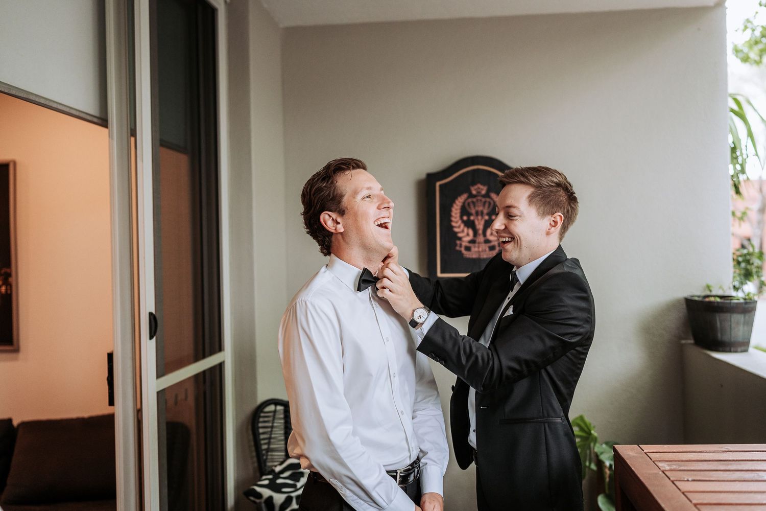 Two people share a joyful moment together while sitting near a window in casual attire.