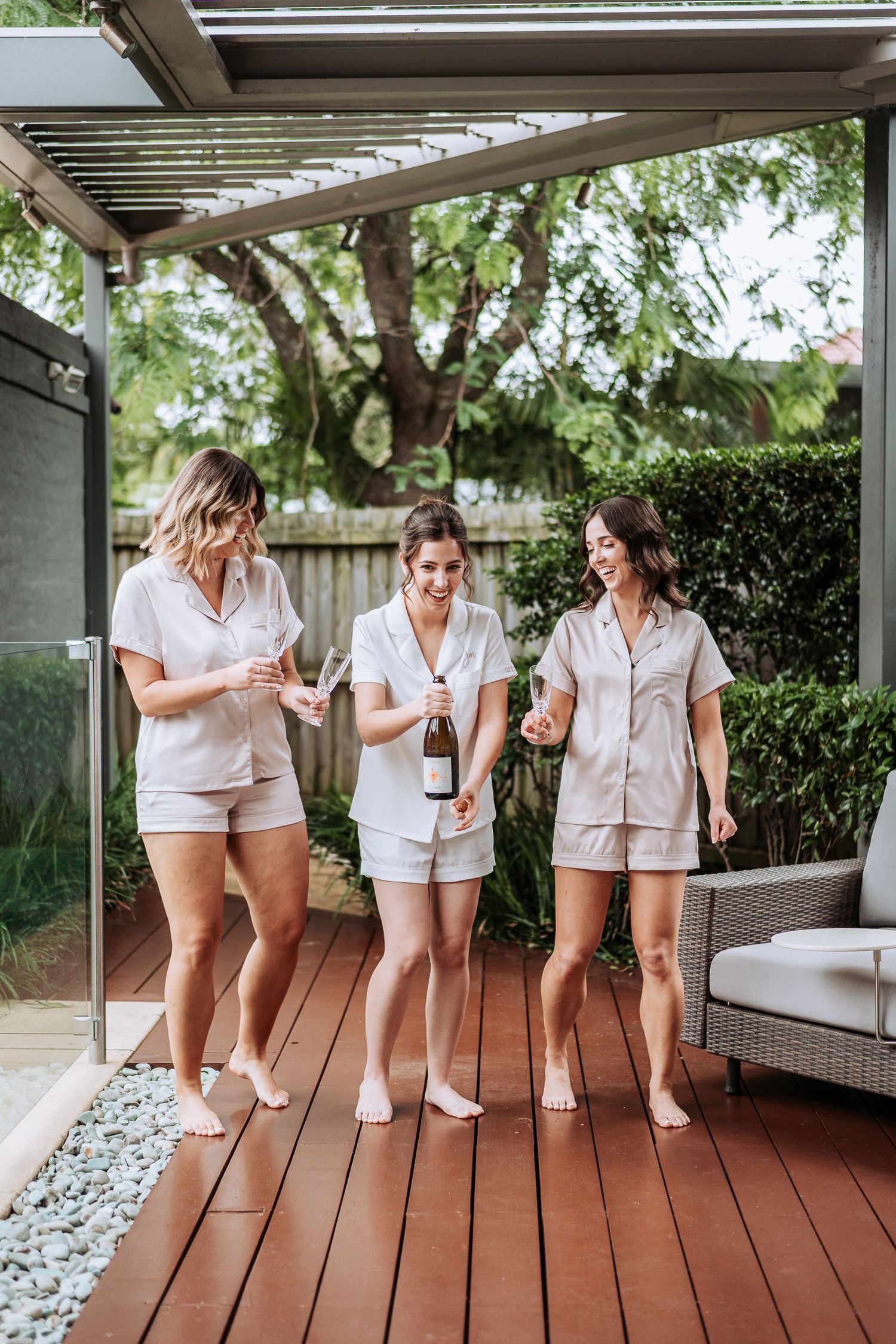 A group in matching white outfits sits together on a wooden deck while enjoying champagne and laughter.