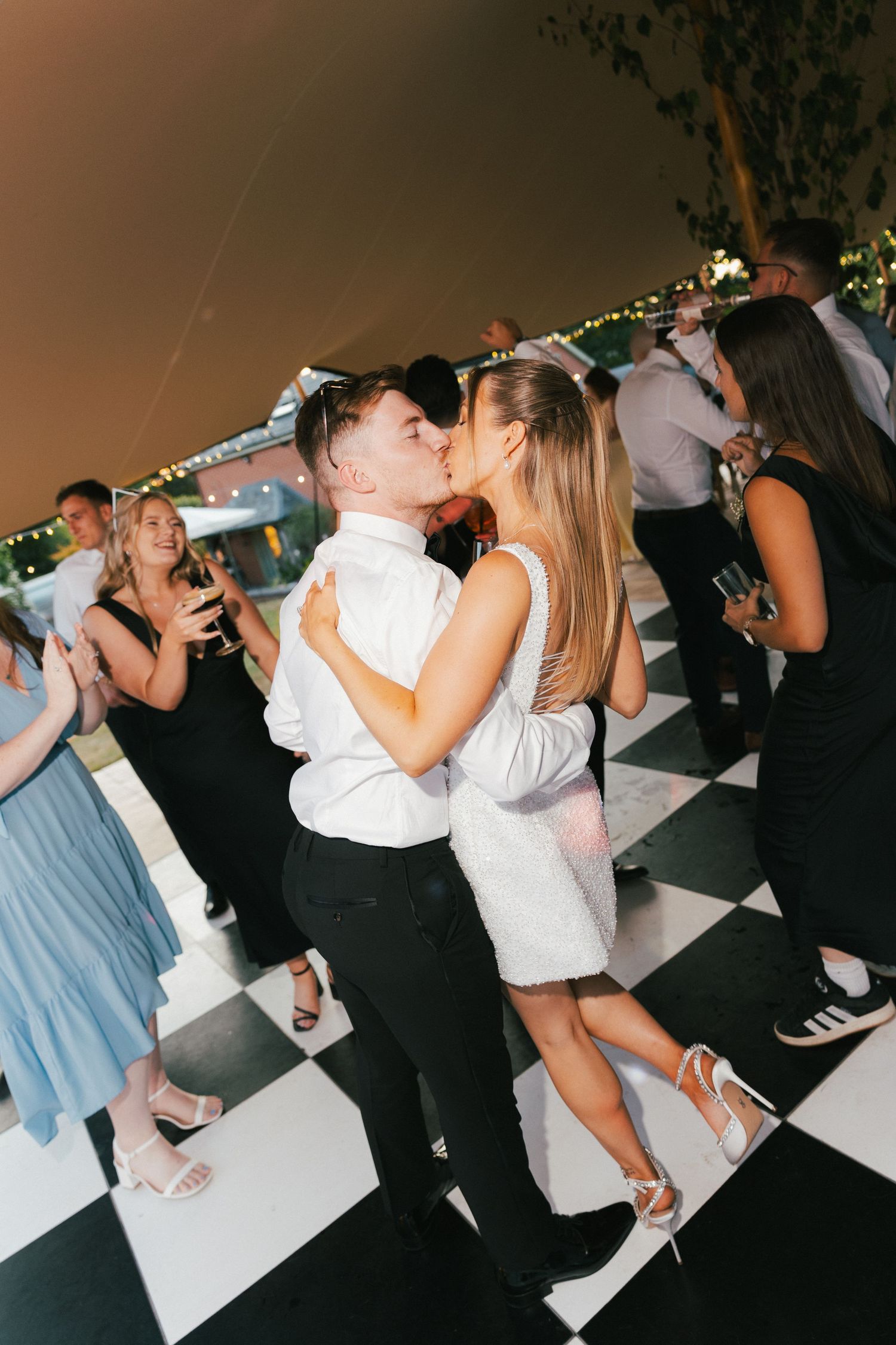 Couples dancing together on a black and white checkered floor under party lights.