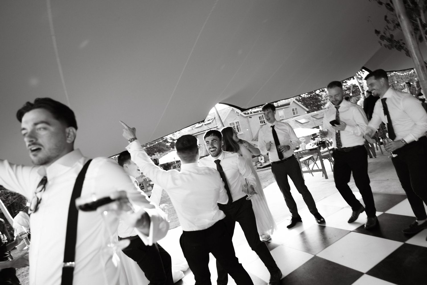 A panoramic black and white sequence of guests dancing at an outdoor celebration.