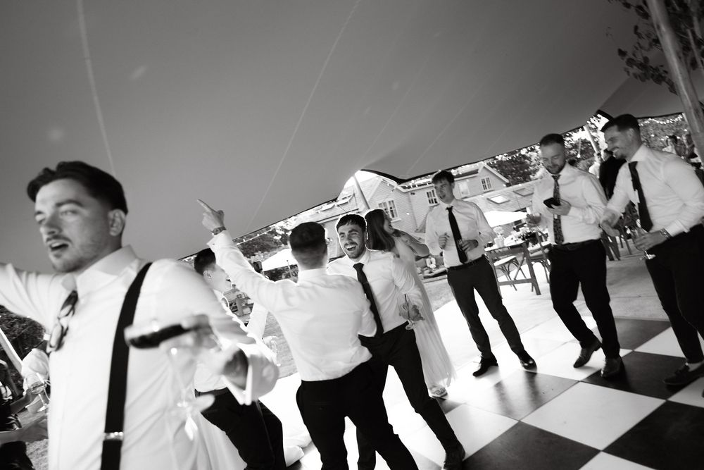 A panoramic black and white sequence of guests dancing at an outdoor celebration.