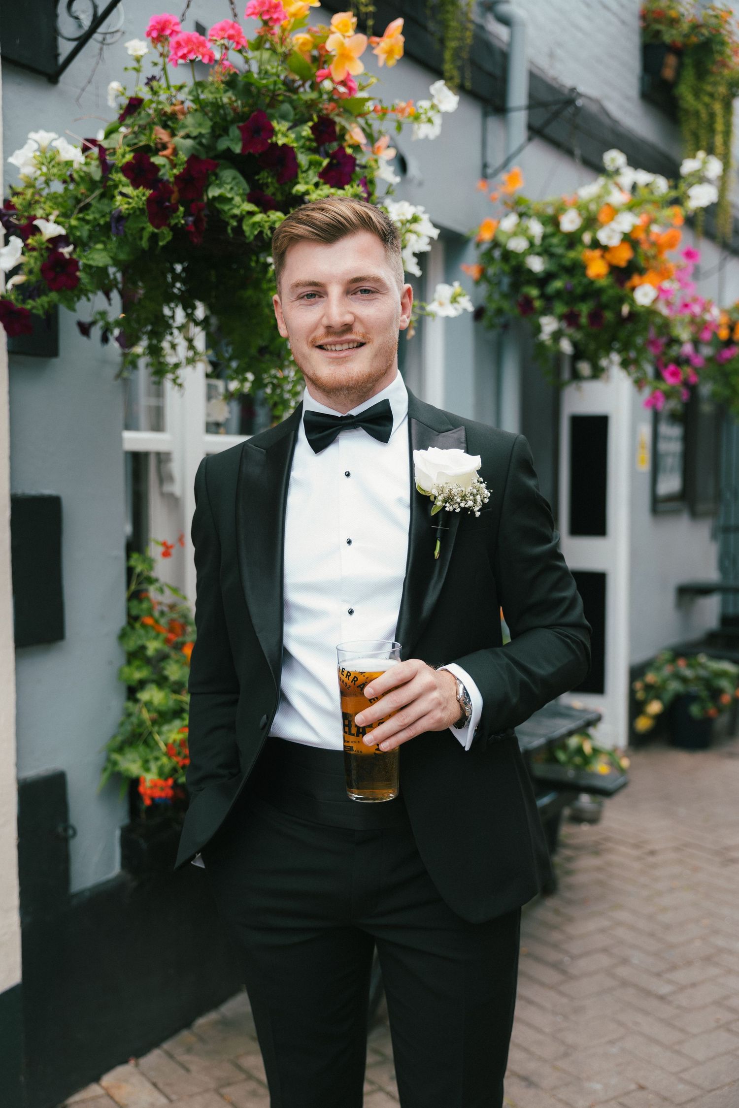 Formal wedding attire and celebratory drink against backdrop of colorful flowers.