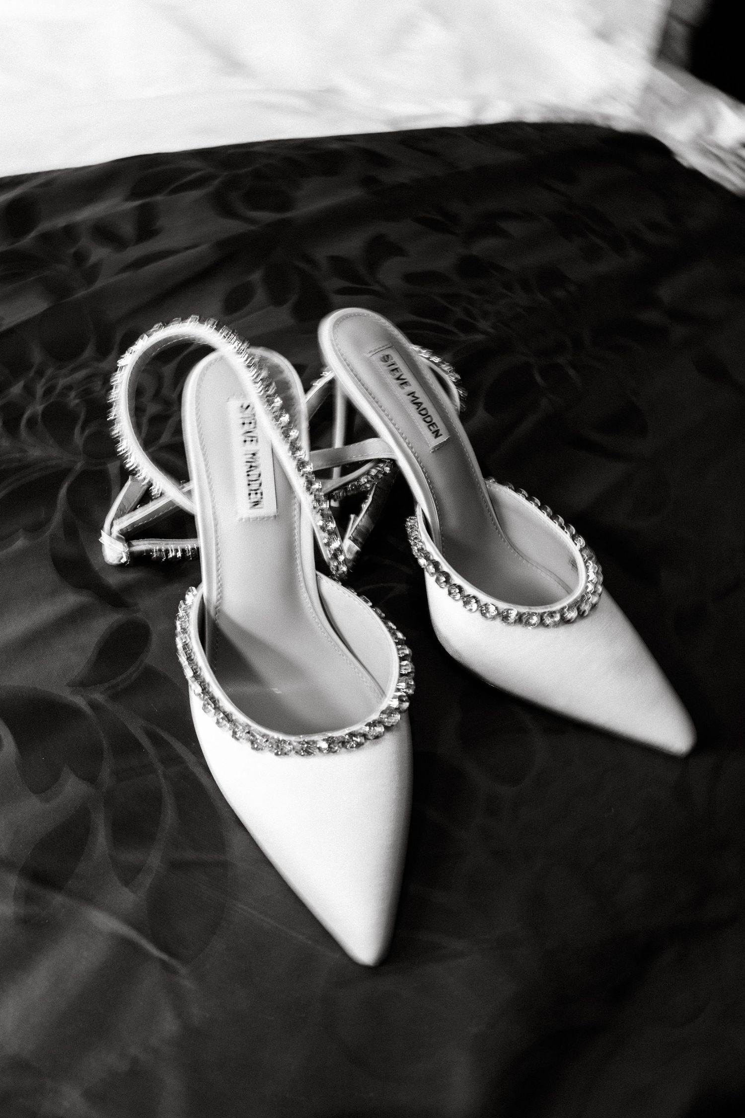 Elegant white bridal shoes with pearl trim on dark fabric.