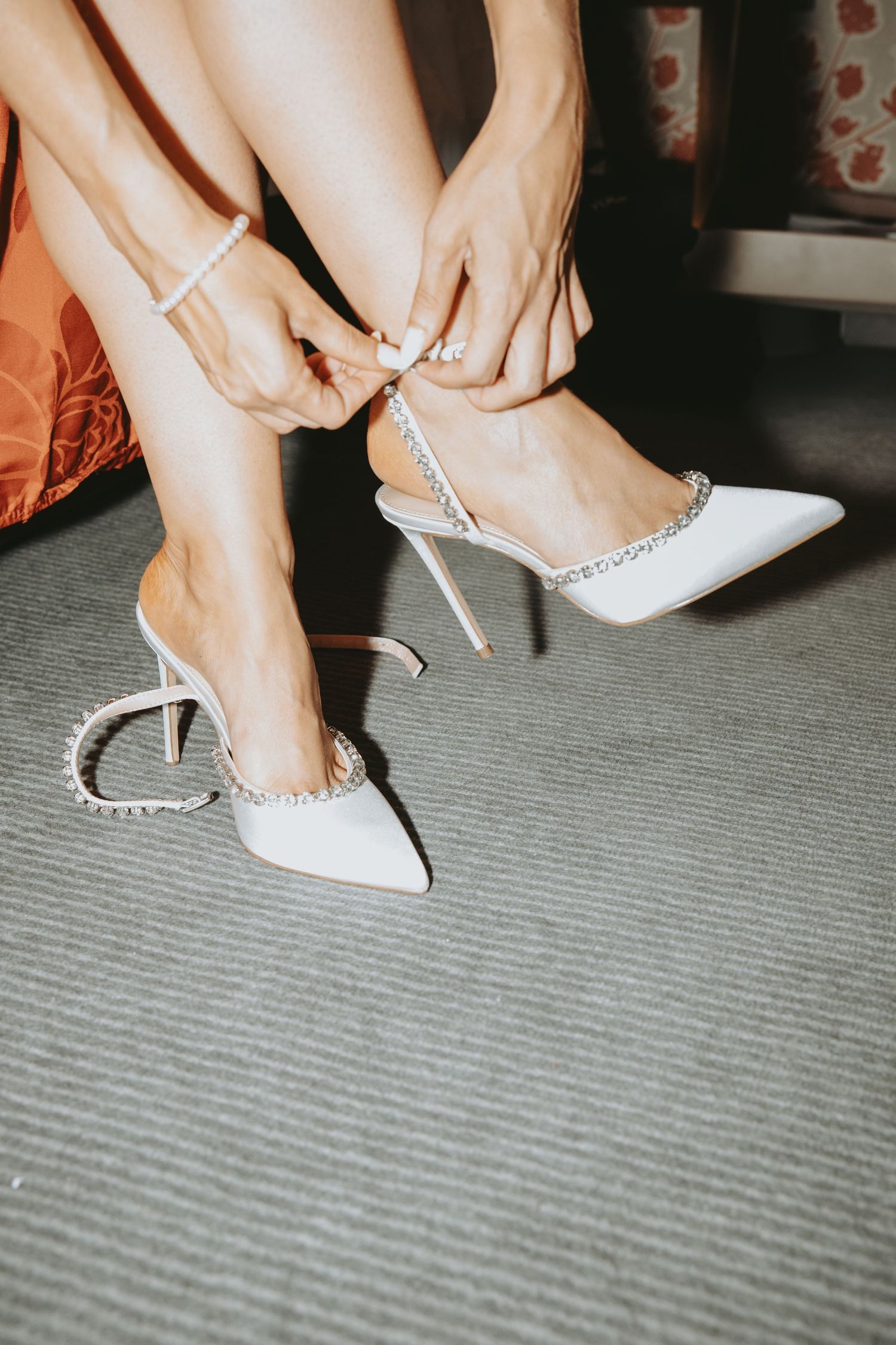 Close-up of hands fastening elegant white bridal shoes with pearl details.