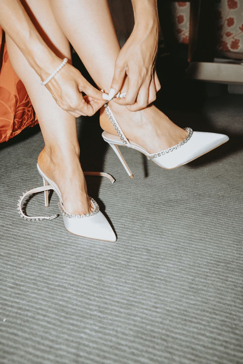 Close-up of hands fastening elegant white bridal shoes with pearl details.