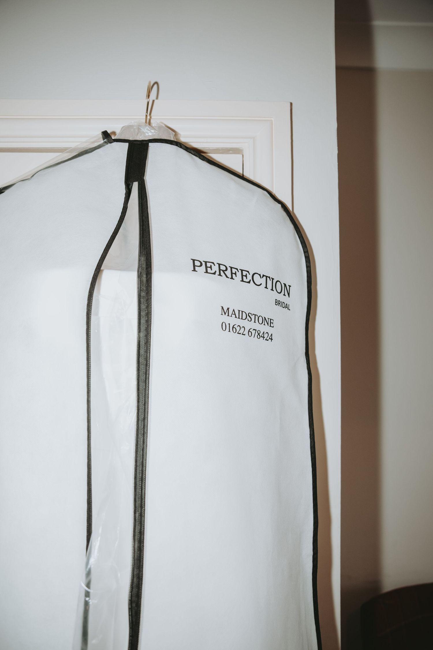 White garment bag labeled 'Perfection' hanging on door.