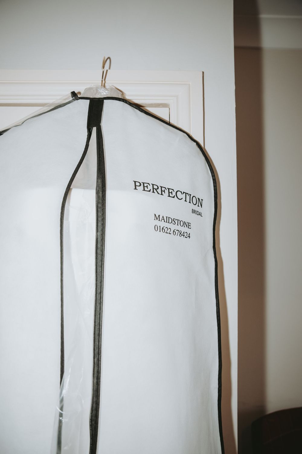 White garment bag labeled 'Perfection' hanging on door.