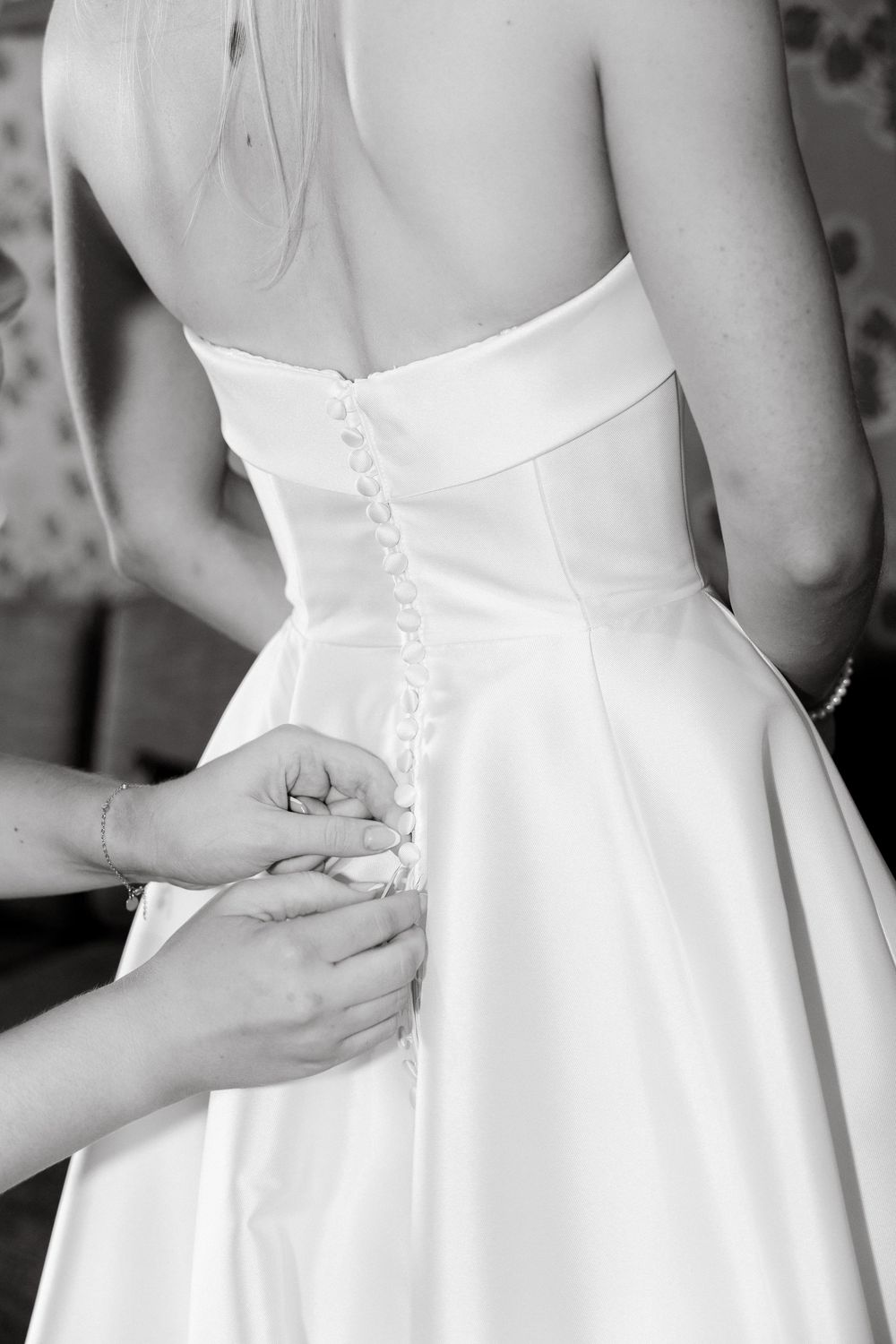 Close-up of hands buttoning up back of white wedding dress.