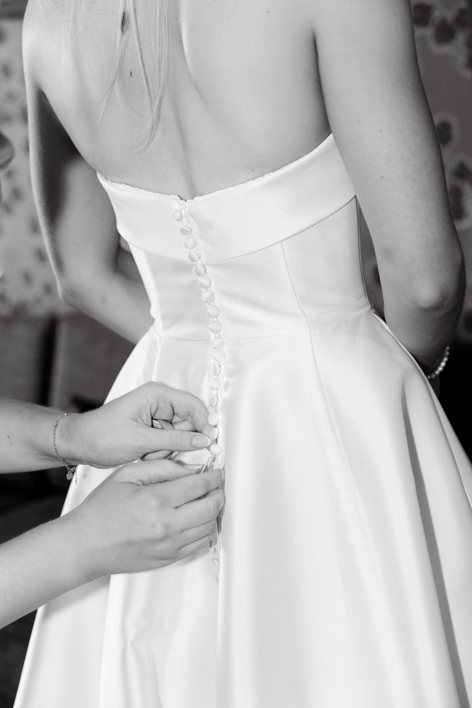Close-up of hands buttoning up back of white wedding dress.