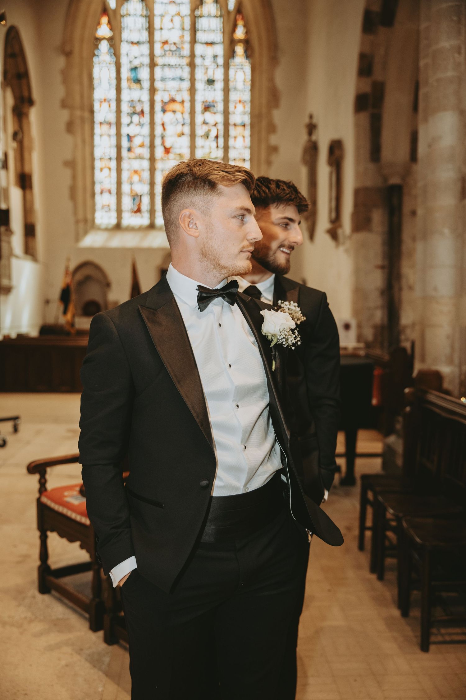 Wedding party members in formal attire stand inside a grand church with stained glass windows.