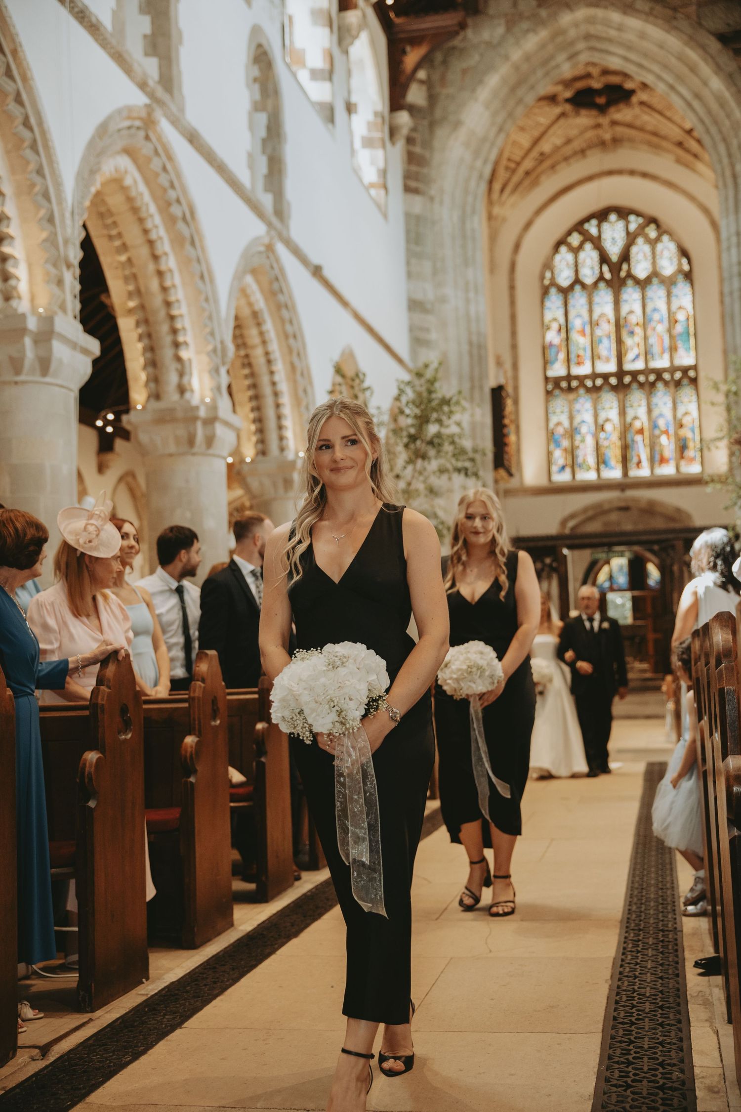 Wedding attendees in formal attire stand along church pews under Gothic arches.