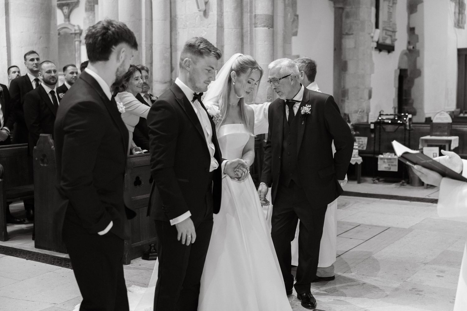 A wedding party celebrates in a grand church hall with stone columns and arched windows.