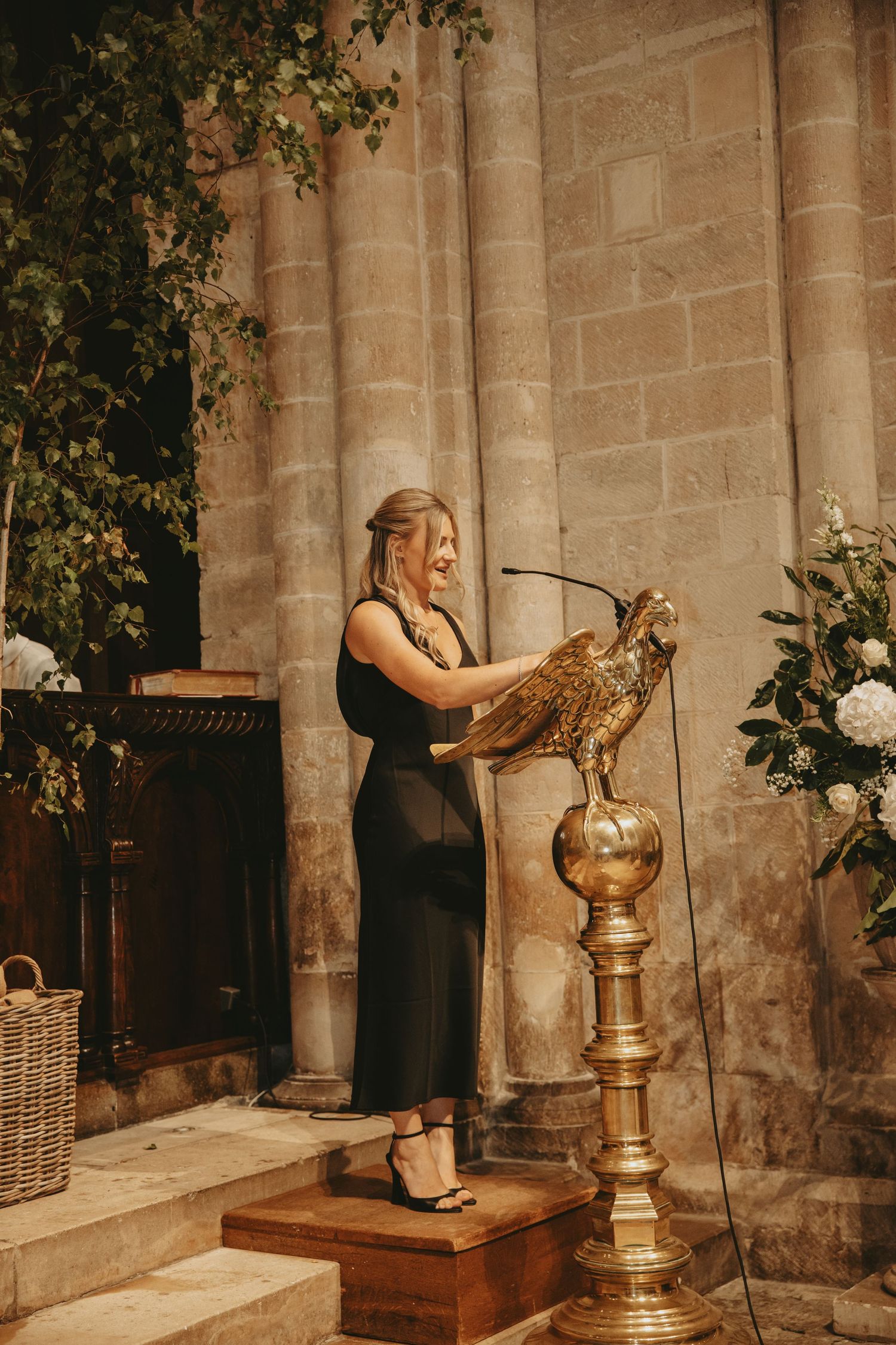 A woman in black interacts with an owl perched on a wooden stand in a historic stone church.