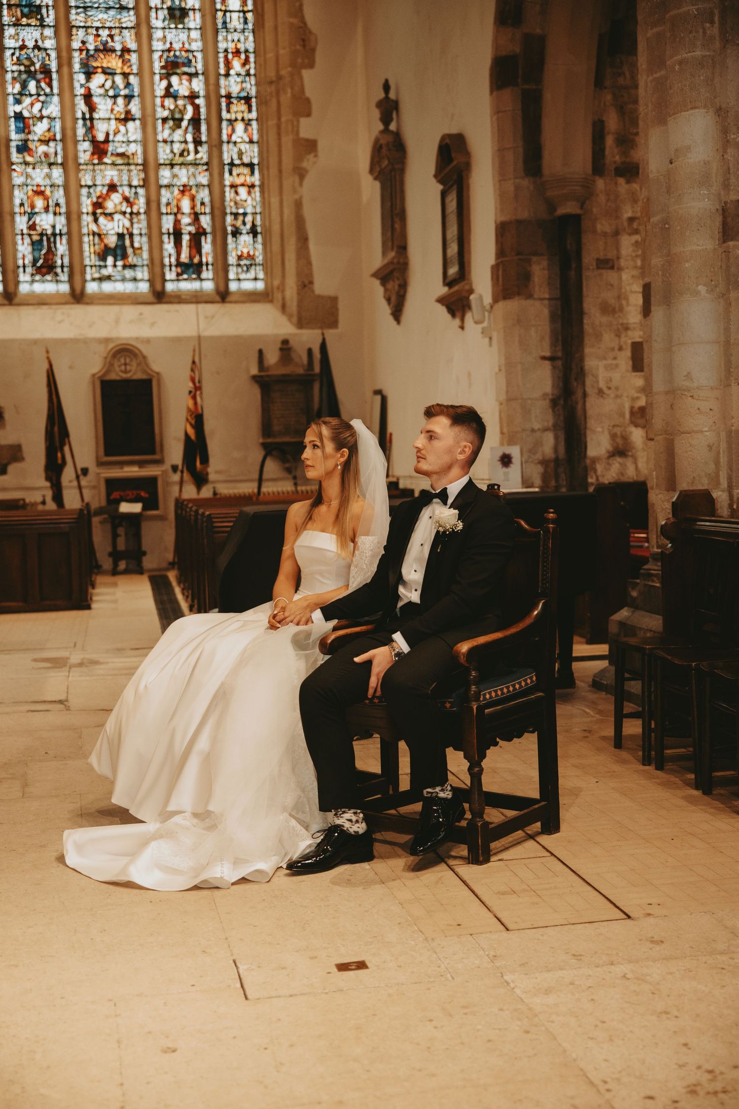 A couple relaxes on wooden benches inside a historic church with stained glass windows.