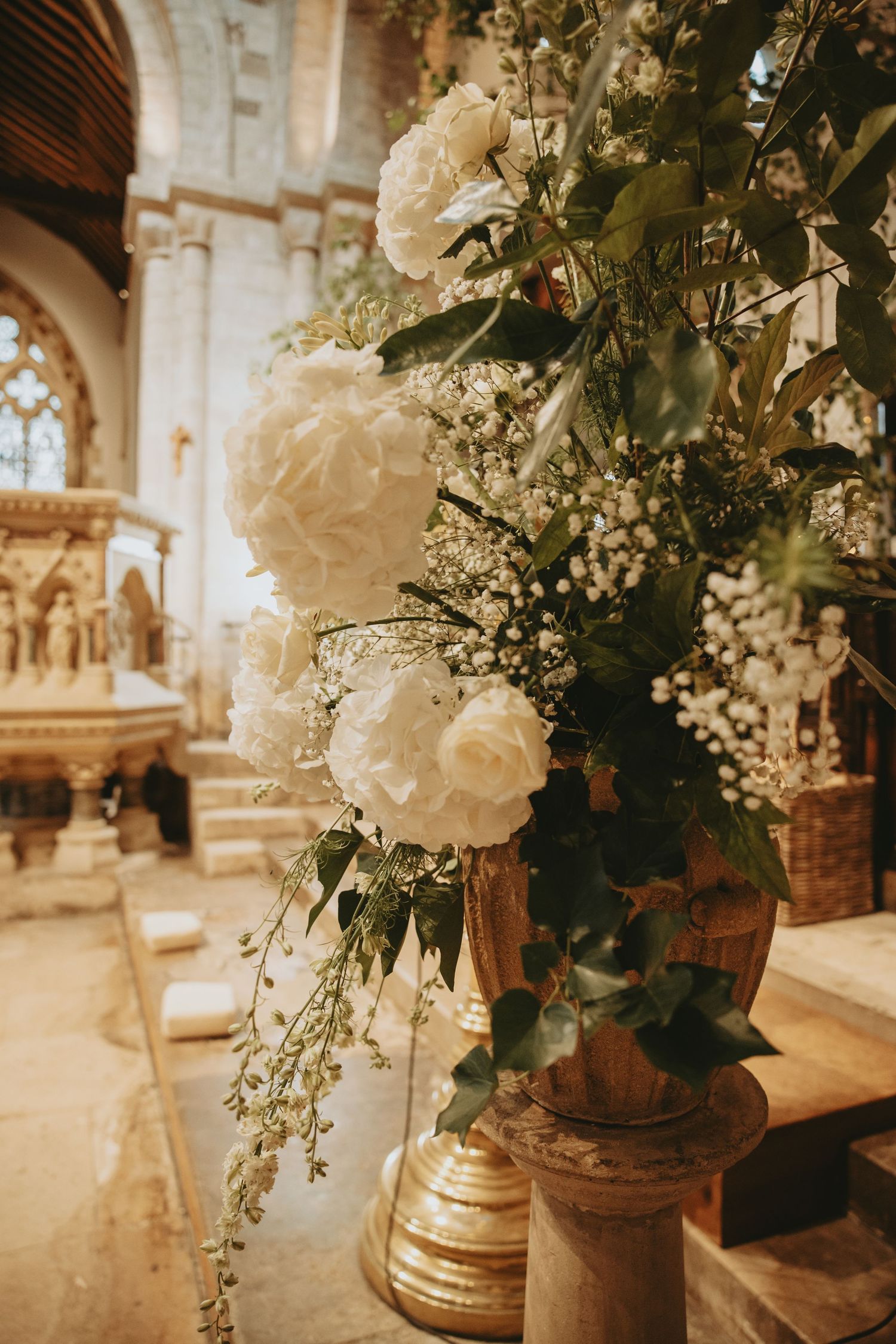 White floral arrangements in gold vases decorate a church interior.