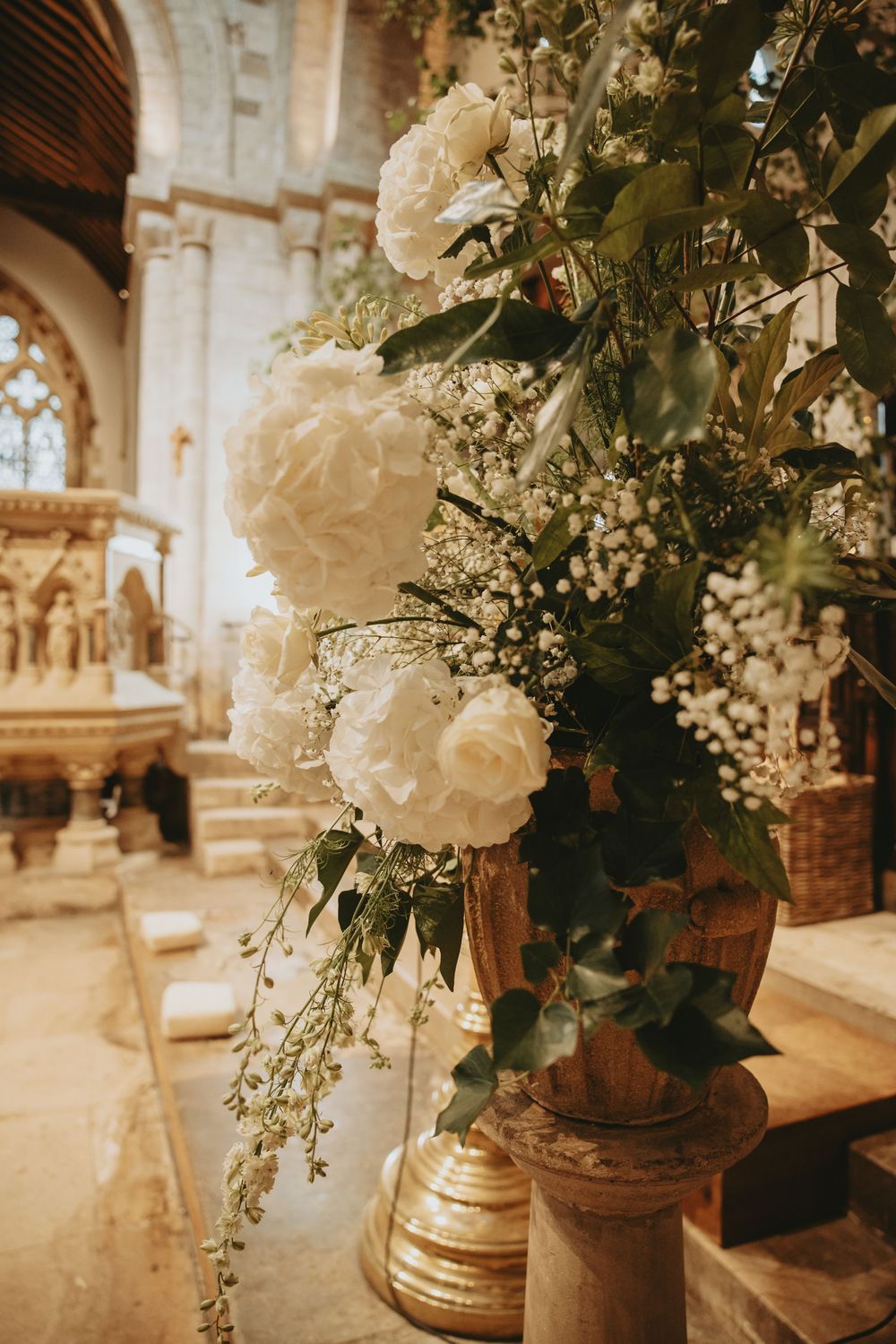White floral arrangements in gold vases decorate a church interior.