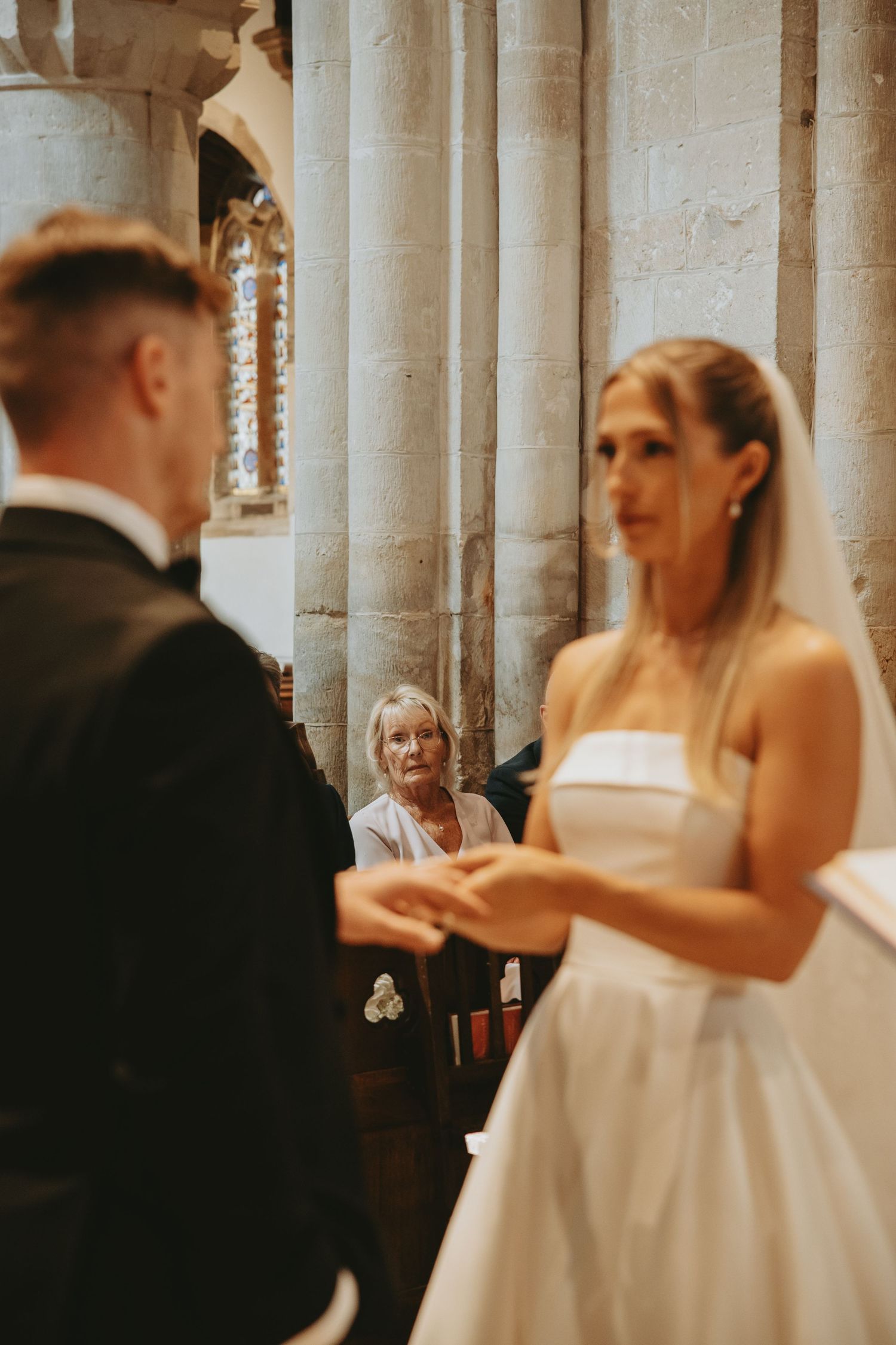 Wedding ceremony participants gather in an ornate church with stone pillars.