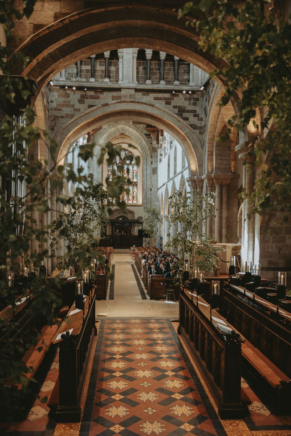 Gothic church interior with wooden pews and decorative floor tiles illuminated by natural light.