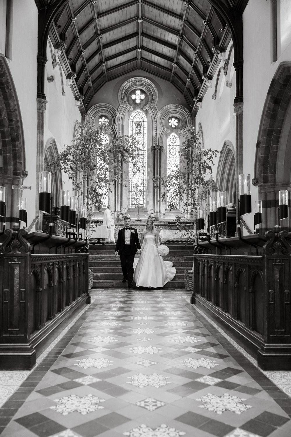 Black and white photo of a church aisle with geometric floor patterns and natural light streaming in.