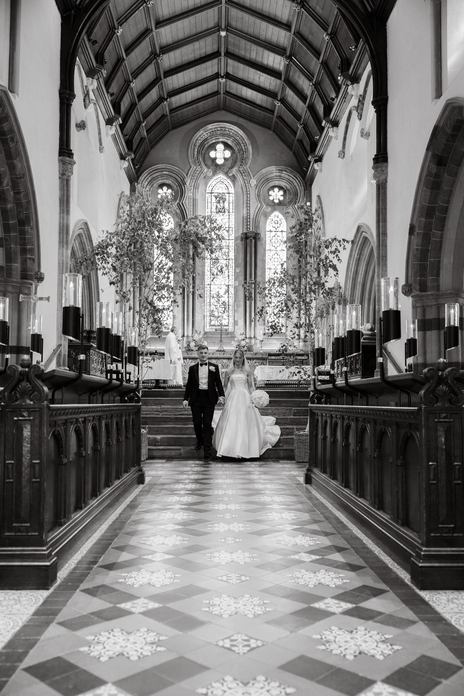 Black and white photo of a church aisle with geometric floor patterns and natural light streaming in.