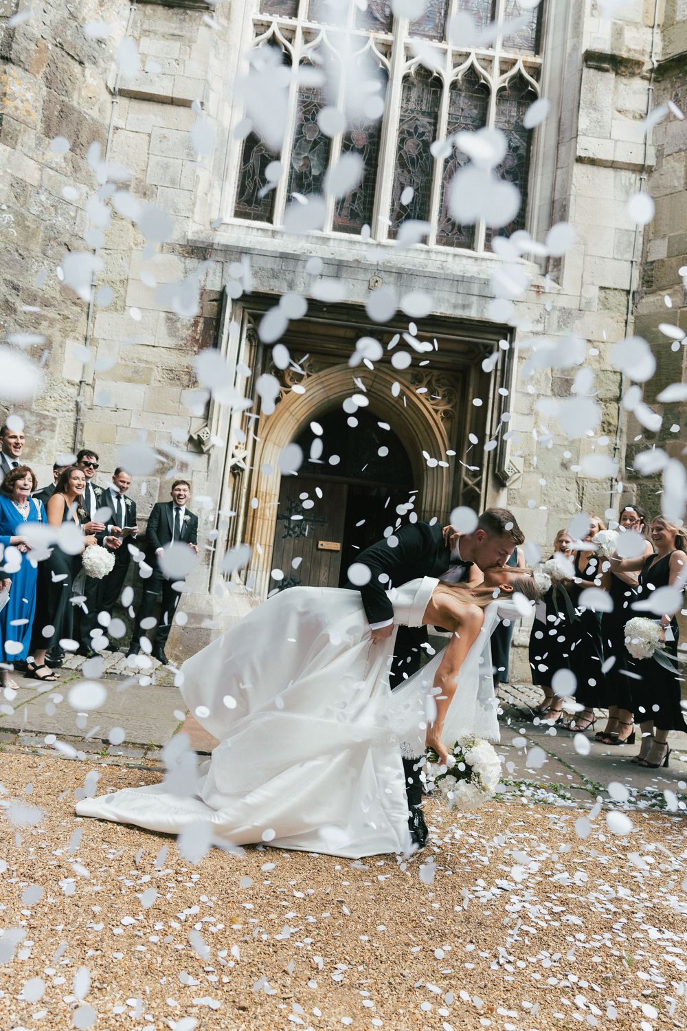 Confetti celebration outside stone church entrance with flowing white dress in motion.